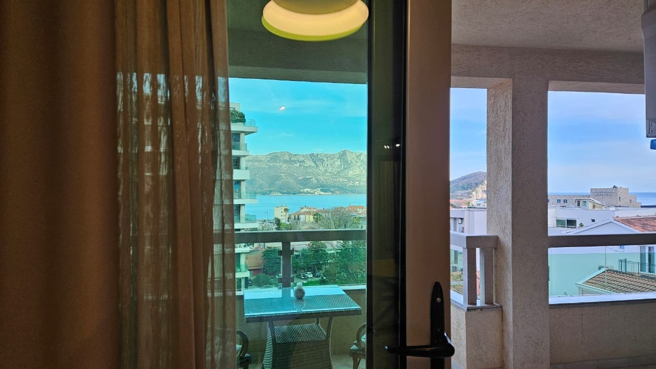 Pogled sa balkona stana u Budvi, Crna Gora: pleteni nameštaj, panoramski pogled na more i planine, moderna završna obrada.