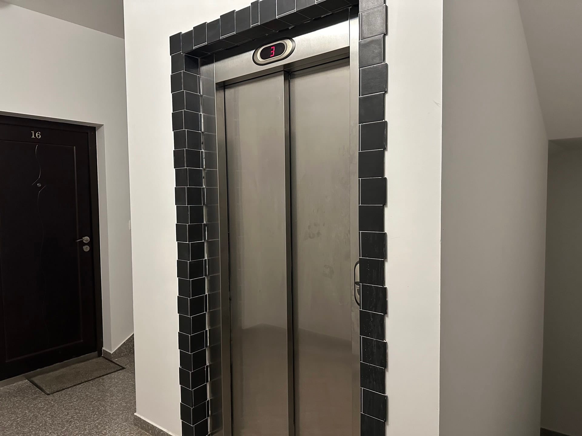 Moderan lift sa oblogom od crnih pločica u ulazu stambene zgrade u Budvi, Crna Gora.