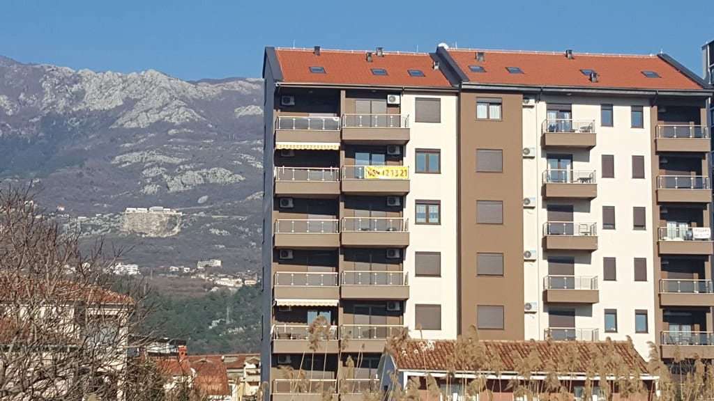 Savremena višespratnica sa balkonima u Budvi, Crna Gora, u pozadini slikovitog planinskog pejzaža.