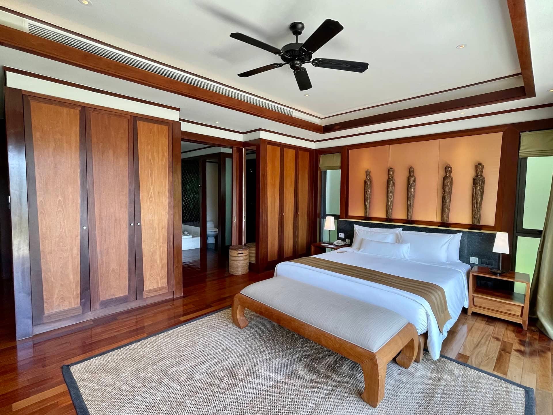 Интерьер спальни с деревянной отделкой, большой кроватью и потолочным вентилятором в апартаментах на Пхукете, Таиланд