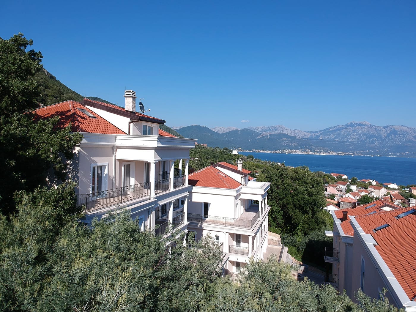 Savremene vile sa crvenim krovovima i pogledom na more u Kumboru, Crna Gora, okružene zelenilom i planinama.