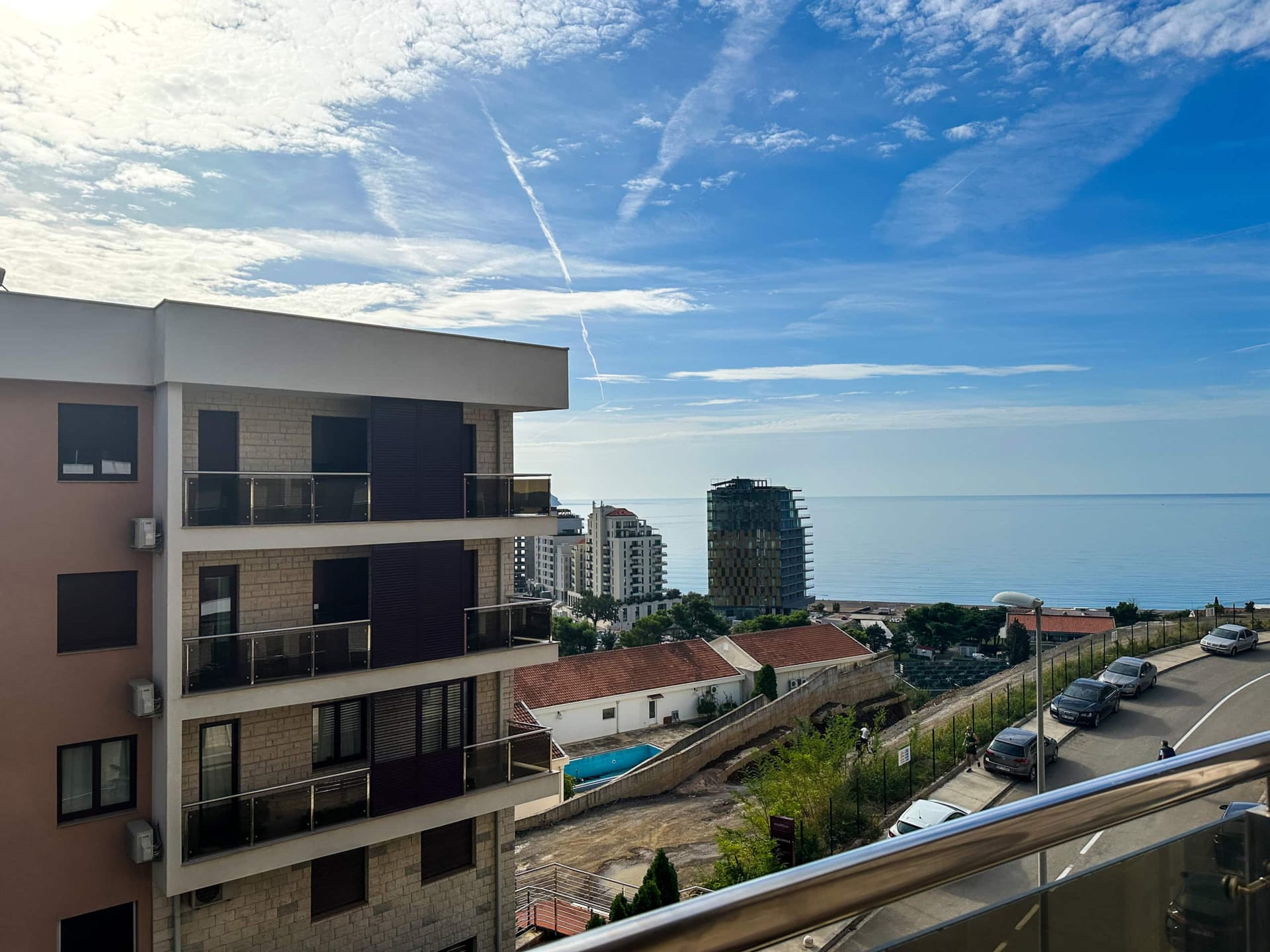 Pogled sa balkona modernog stana u Bečićima, Crna Gora: panorama mora, stambenog kompleksa i obližnjeg puta.