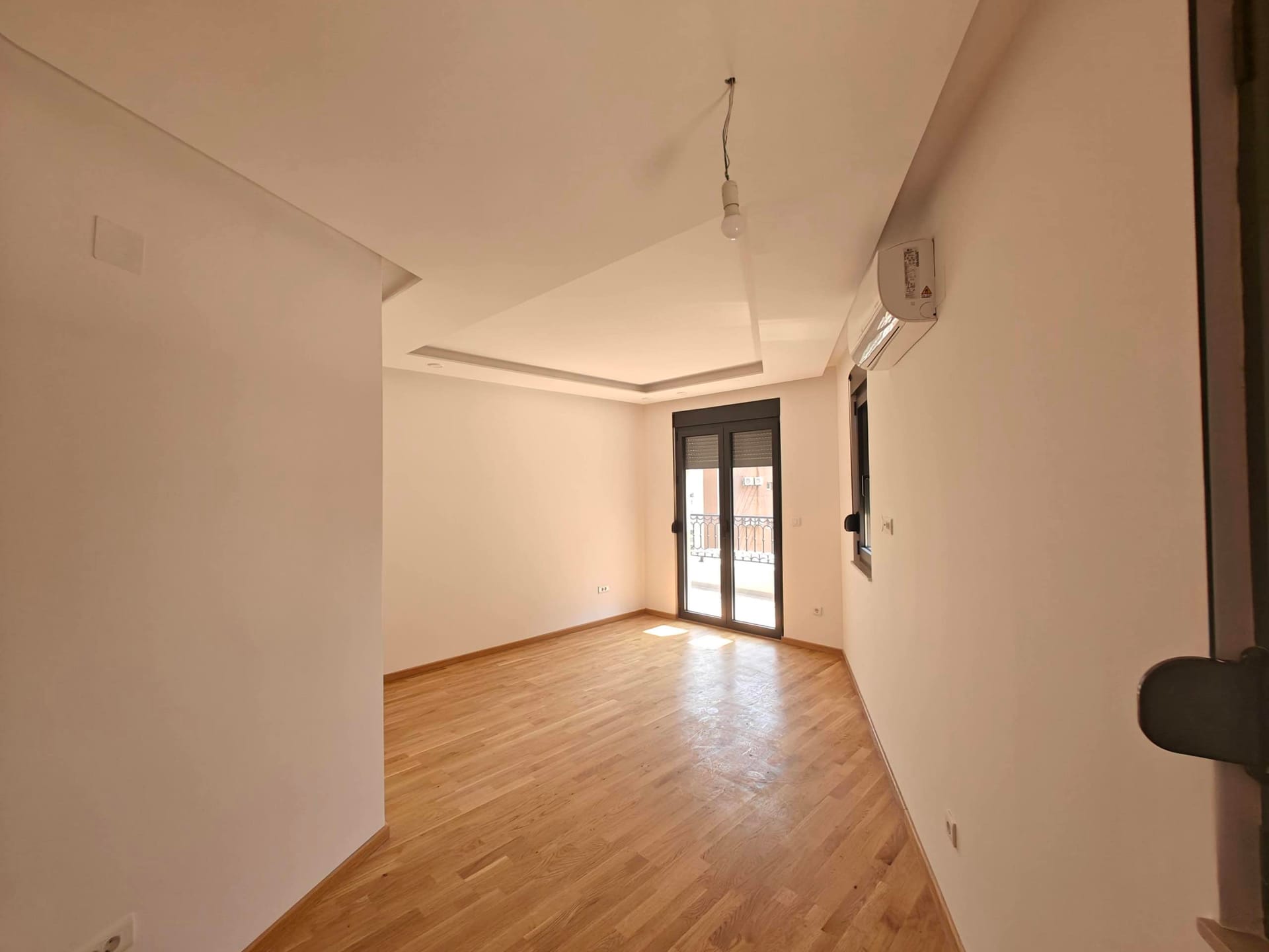Svetao dnevni boravak sa parketom, klima-uređajem i izlazom na balkon u novom stanu, Budva, Crna Gora.