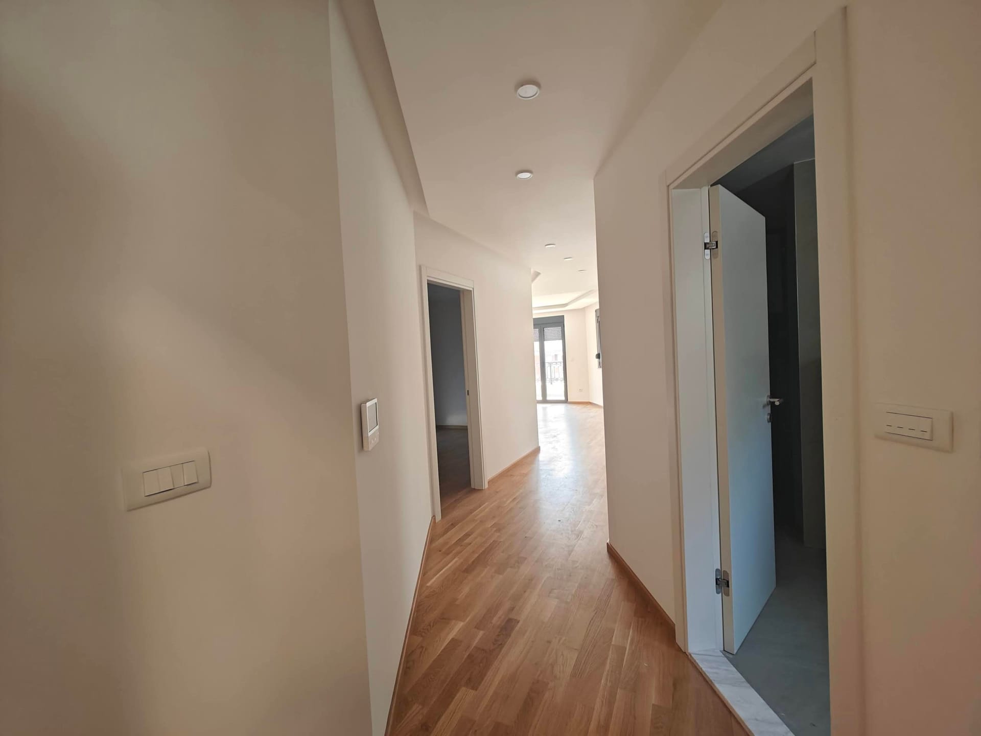 Svetao hodnik u modernom stanu u Budvi, Crna Gora: parket, beli zidovi i ugrađeno osvetljenje.