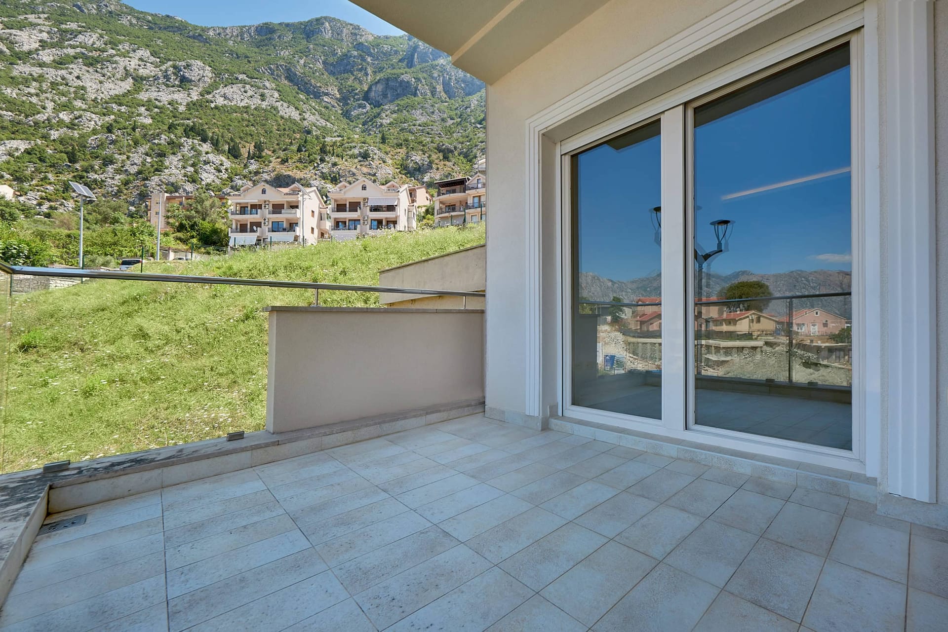 Prostran balkon s panoramskim pogledom na planine u stanu, Dobrota, Crna Gora: pločice na podu i staklena ograda.