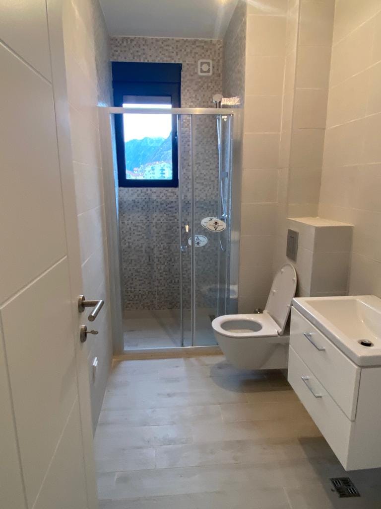 Savremeno kupatilo sa tuš kabinom u stanu, grad Dobrota, Crna Gora: svetle pločice i sanitarije.