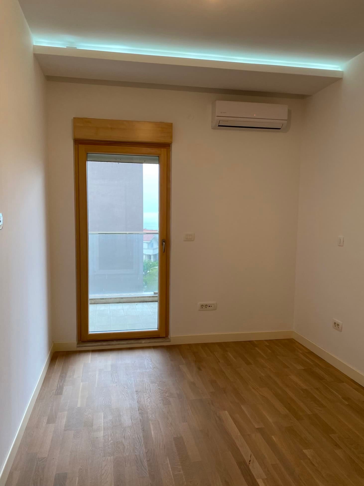 Svetla spavaća soba u stanu, Dobrota, Crna Gora: parket, izlaz na balkon, klima-uređaj i savremena završna obrada.