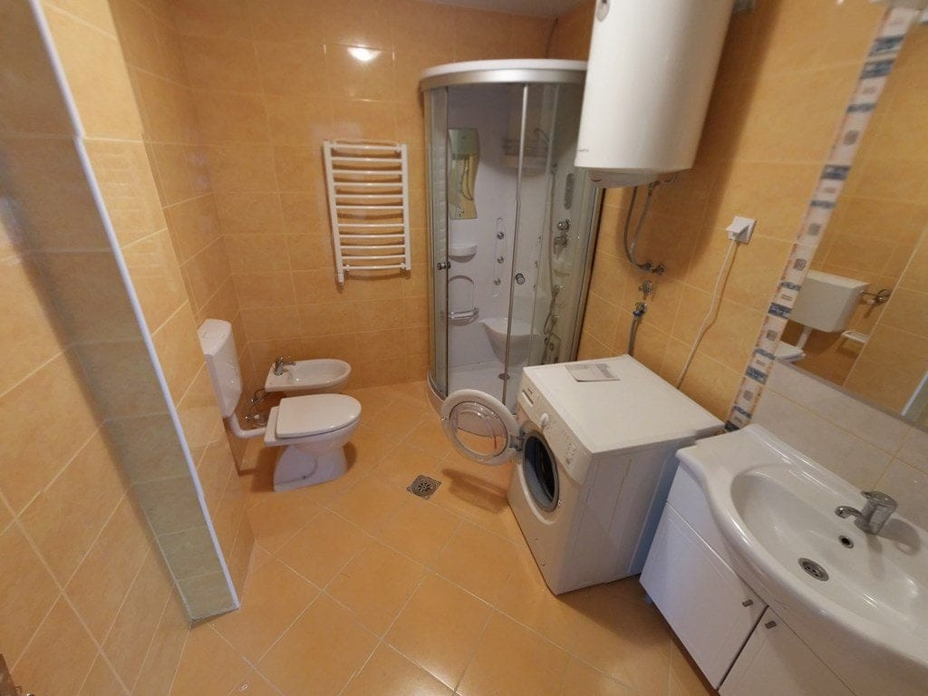 Kupatilo u stanu u Budvi, Crna Gora: tuš kabina, veš mašina, bide i svetle pločice.