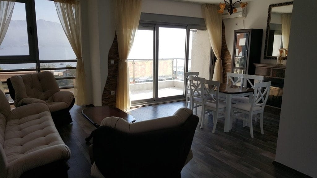 Dnevna soba s pogledom na more u stanu u Budvi, Crna Gora: mekani nameštaj, trpezarijski deo i izlaz na balkon.
