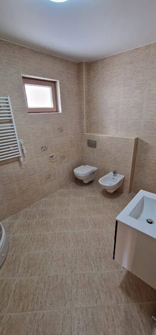 Salle de bain moderne dans un appartement à Bečići, Monténégro : WC suspendu, bidet, carrelage beige et fenêtre.