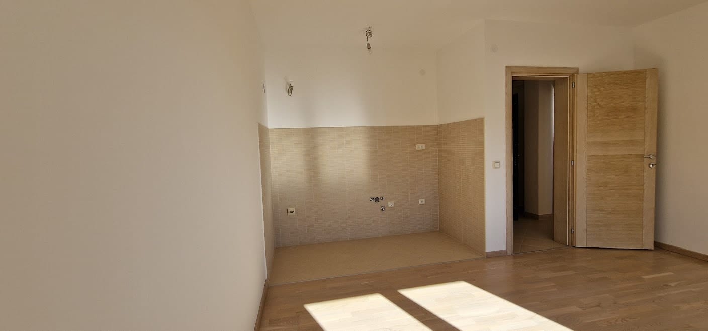 Zone cuisine dans un appartement à Bečići, Monténégro : finitions claires, crédence en carrelage, parquet et porte intérieure.