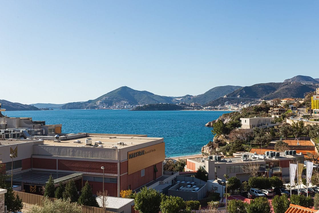 Panoramski pogled na more i hotel Maestral u Pržnu, Crna Gora: slikovita uvala, planine i plaža sa terase stana.