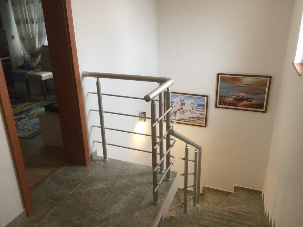 Stepenište sa metalnim ogradama u dvosobnom apartmanu u gradu Bar, Crna Gora, sa slikama na zidovima.