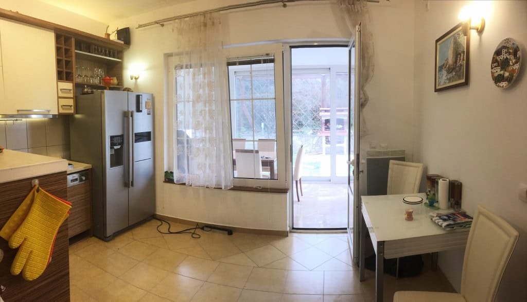 Kuhinja sa trpezarijskim delom u apartmanu u gradu Bar, Crna Gora: svetao nameštaj, izlaz na terasu i pogled na baštu.