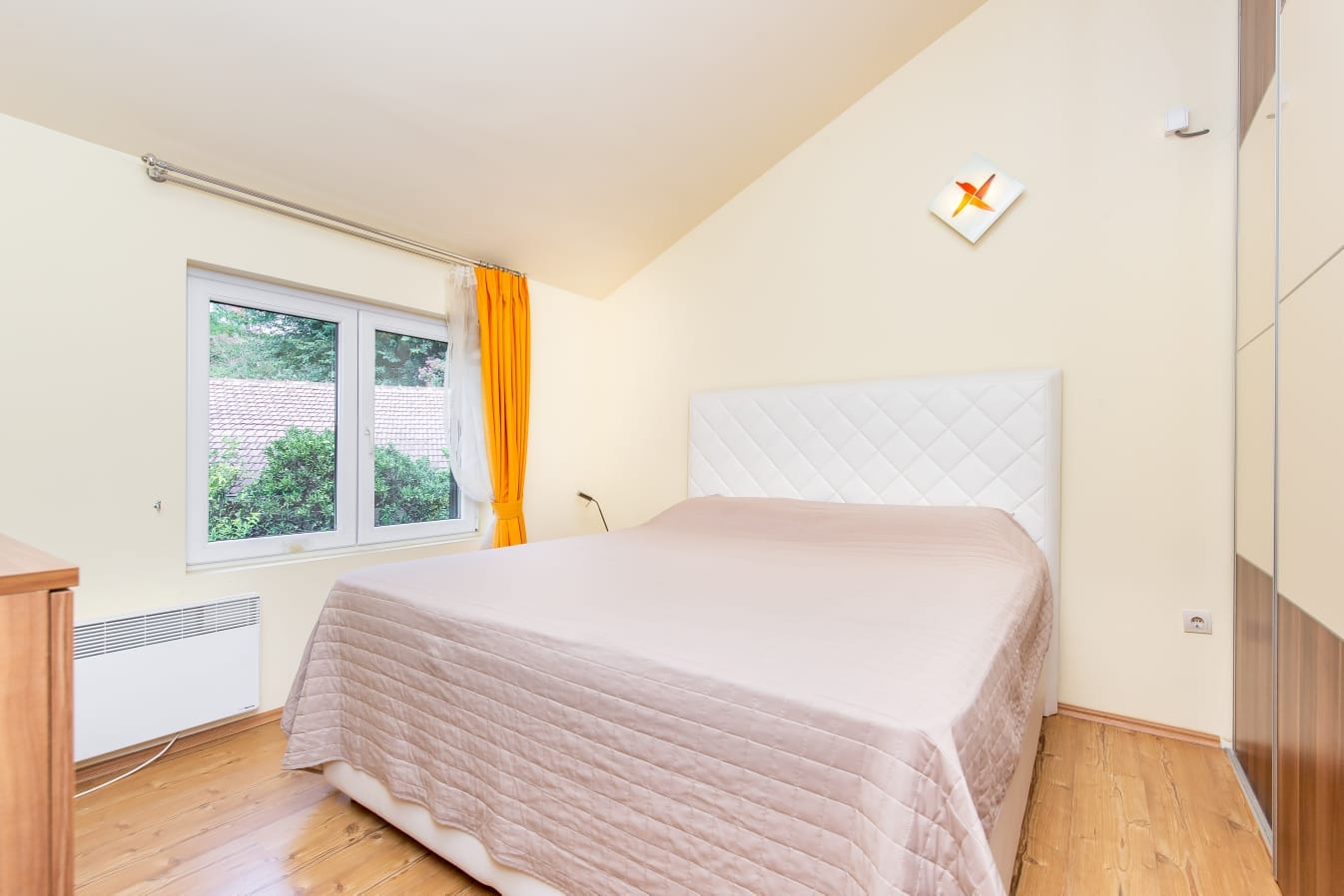Helles Schlafzimmer mit Doppelbett und Kleiderschrank in einer Wohnung in Đenovići, Montenegro. Blick ins Grüne aus dem Fenster.
