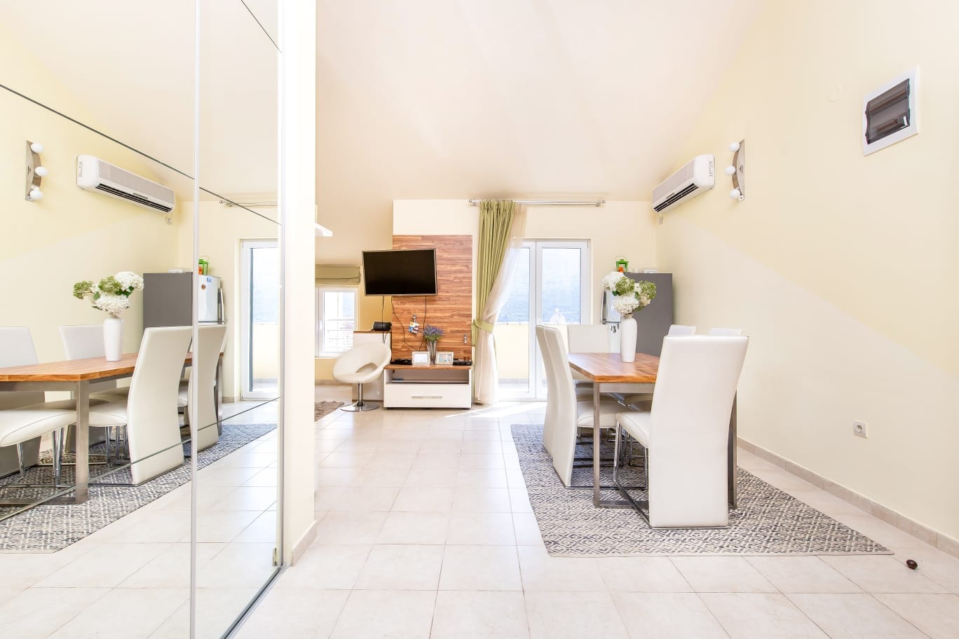 Helles Wohnzimmer mit Essbereich in einer Wohnung in Đenovići, Montenegro: weiße Möbel, Spiegel und Panoramafenster.