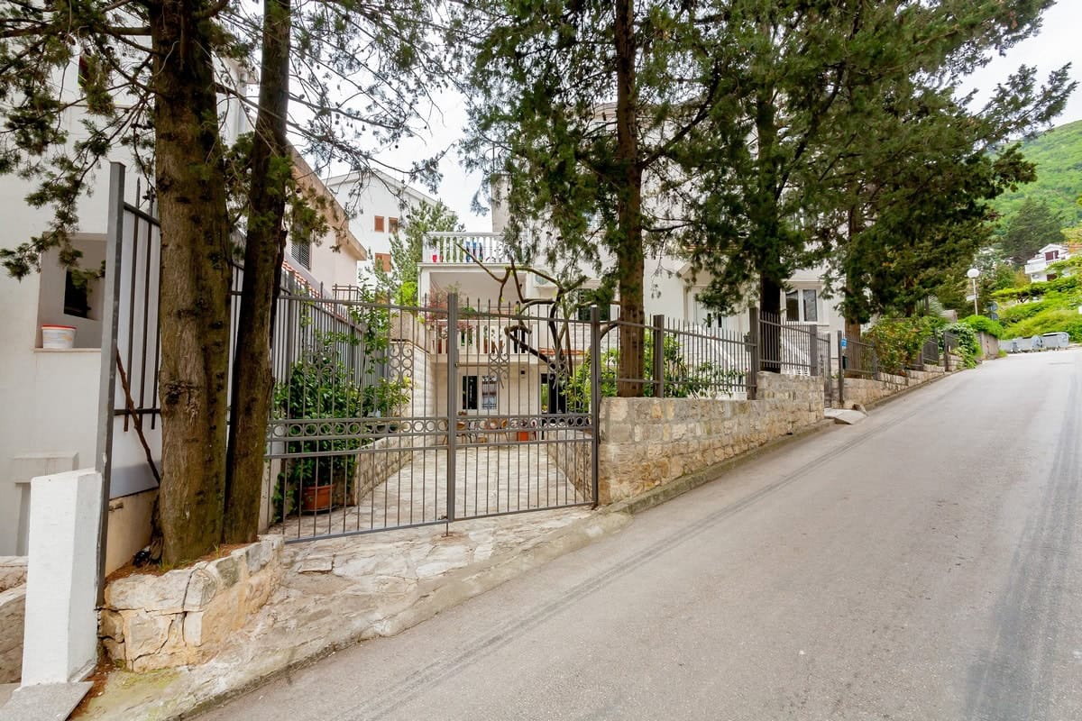Fasada kuće u Budvi, Crna Gora: privatno dvorište sa kovanim kapijama, kamenim ogradama i četinarima.