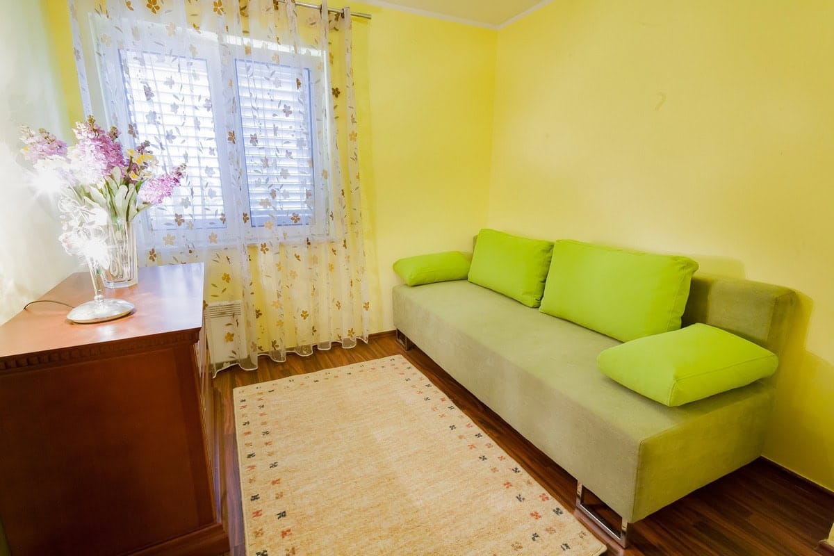 Ugodan dnevni boravak sa zelenom sofom i žutim zidovima u kući na prodaju, Budva, Crna Gora.