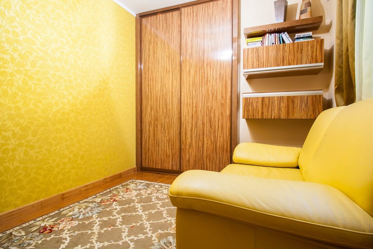 Dnevna soba u kući u Budvi, Crna Gora: žuta kožna sofa, ugradni ormar sa kliznim vratima i zidne police u enterijeru.