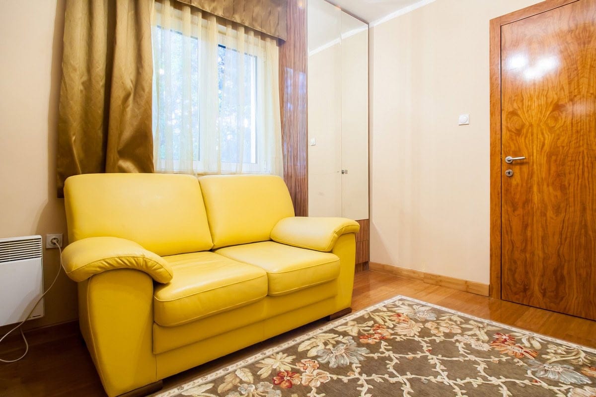 Dnevna soba sa žutom sofom i tepihom u kući na prodaju, Budva, Crna Gora: enterijer sa drvenim vratima i ormarom.