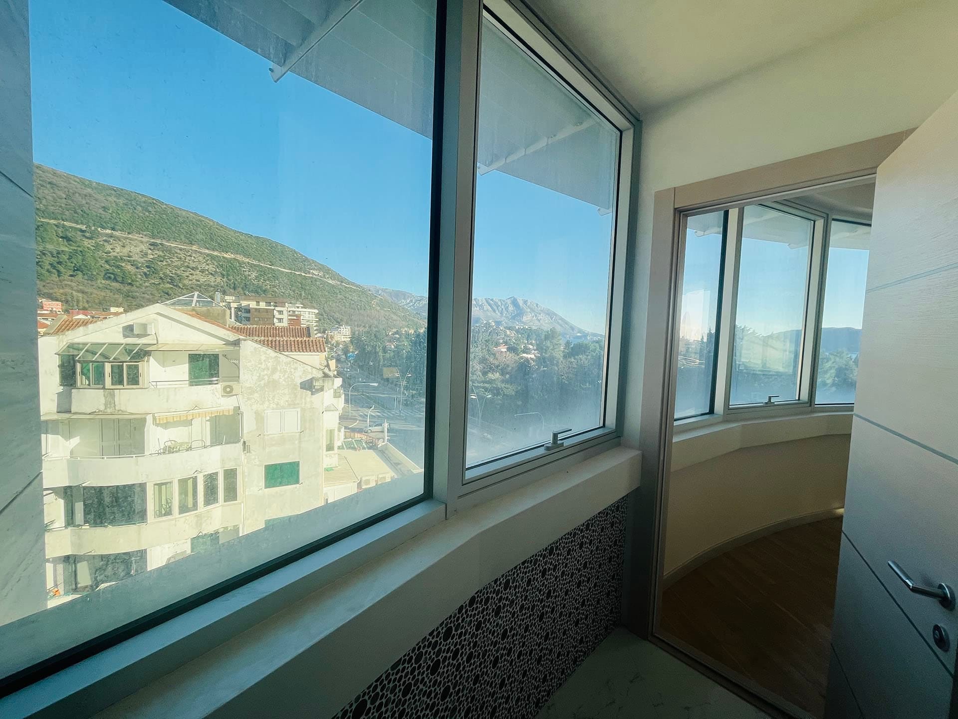 Budva, Karadağ’daki dairenin cam balkonundan dağların ve şehrin panoramik manzarası, modern finisajlı.