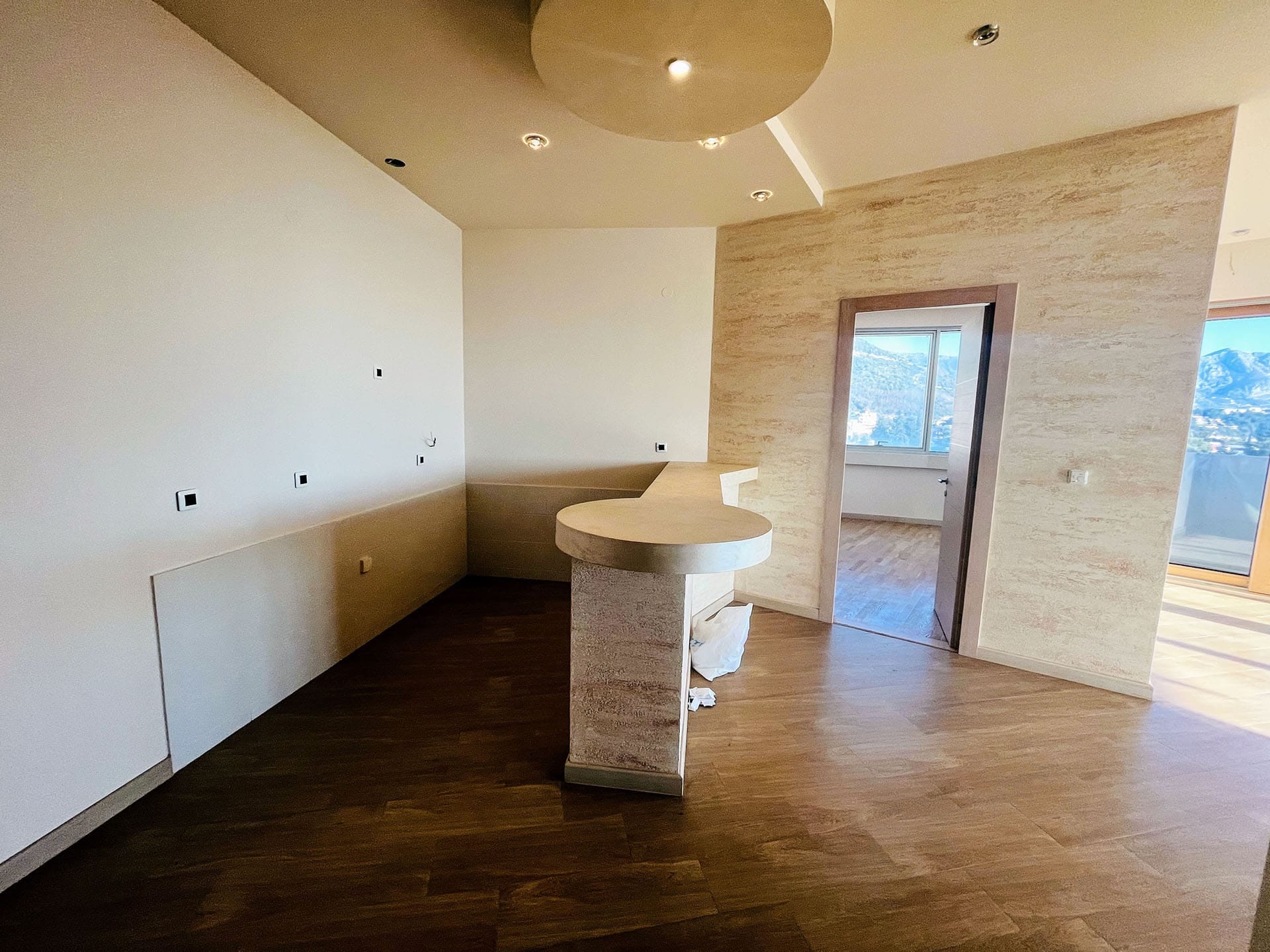 Bar tezgahlı ve dağ manzaralı oturma odası iç mekanı, yeni daire, Budva, Karadağ. Modern duvar kaplaması.