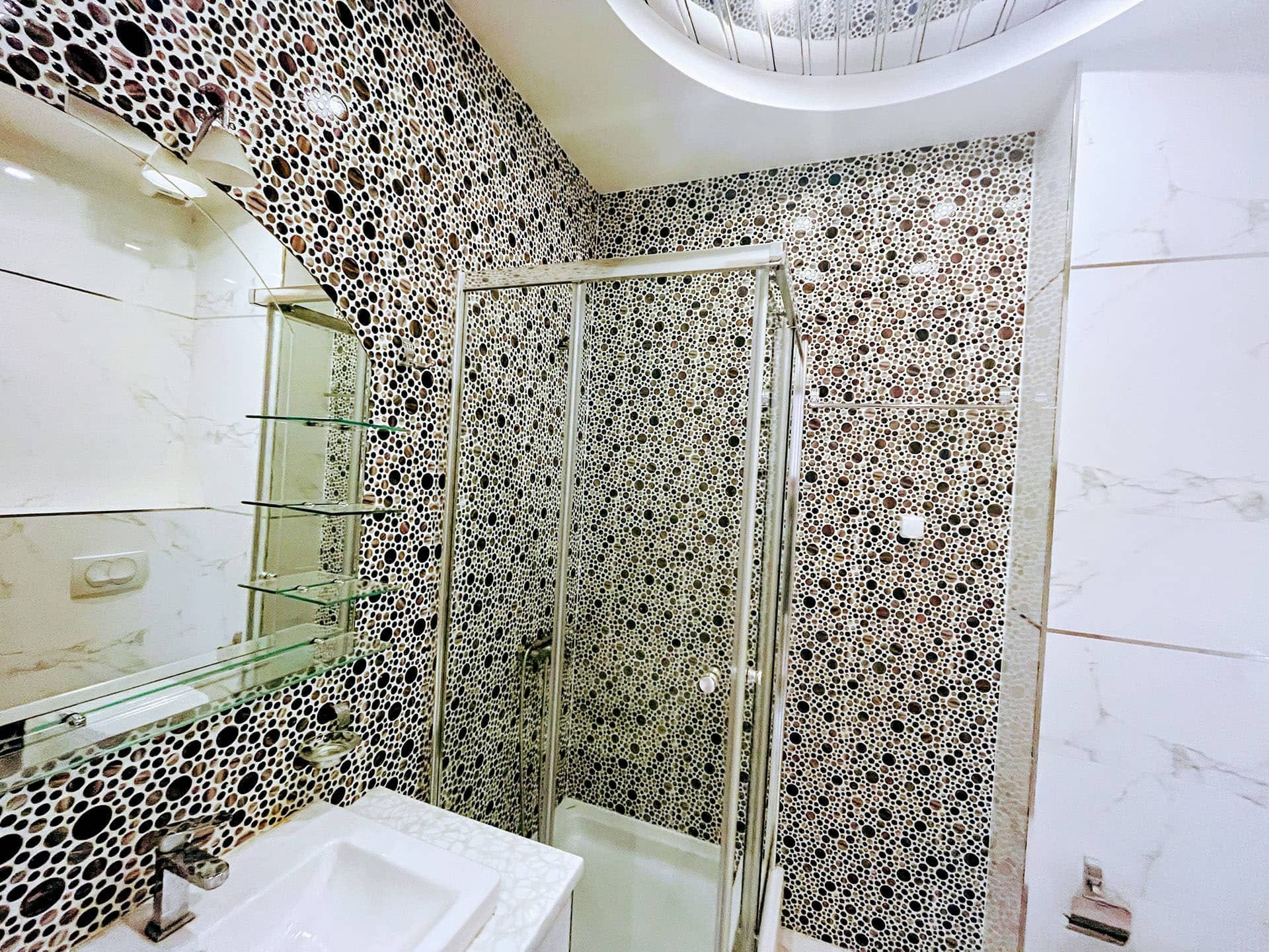 Karadağ, Budva’daki bir dairede modern banyo: duş kabini ve mozaik fayans kaplamalı duvarlar.