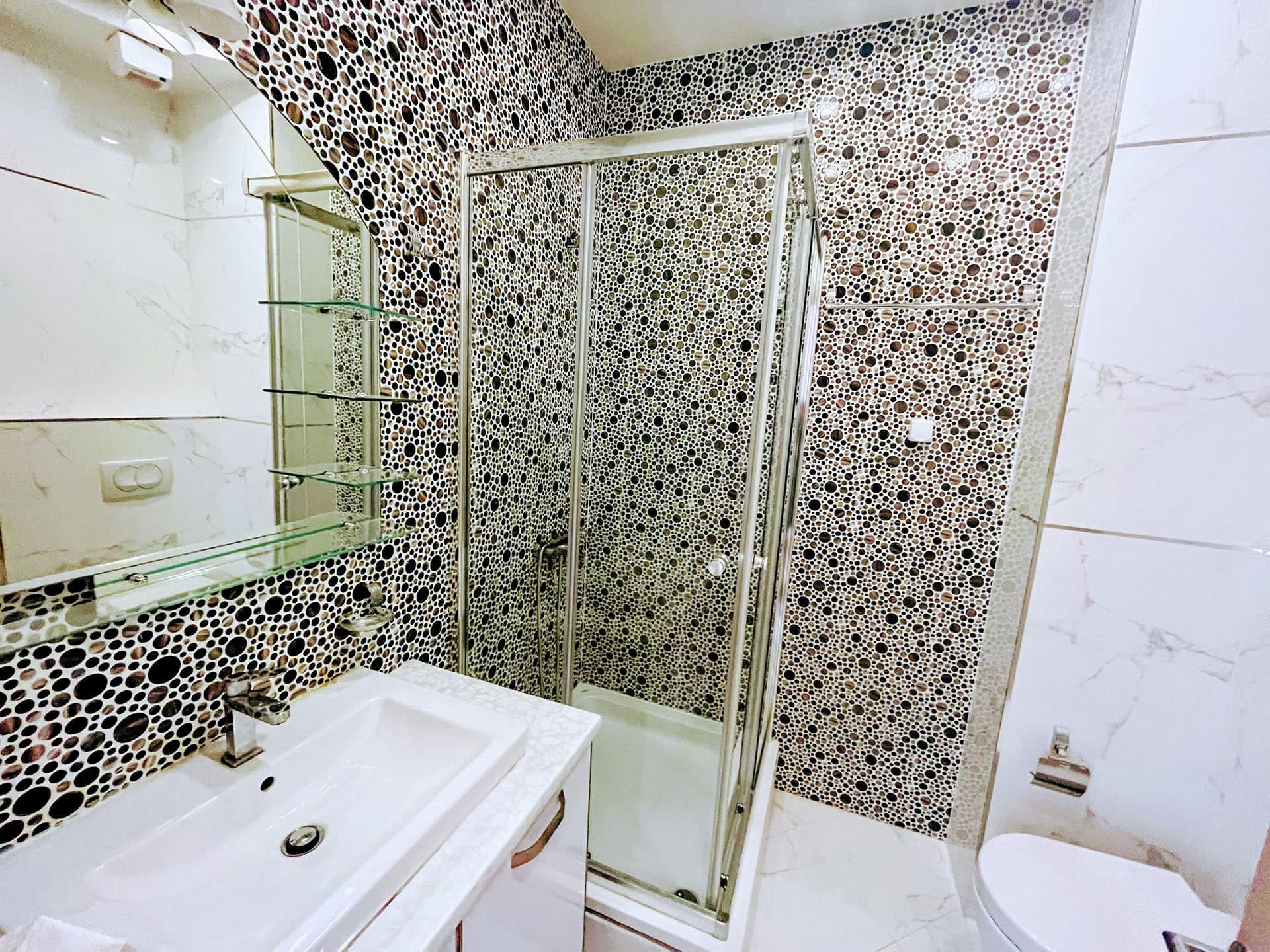Karadağ, Budva’daki bir dairede modern banyo: duş kabini, şık mozaik fayanslar ve beyaz sıhhi tesisat.
