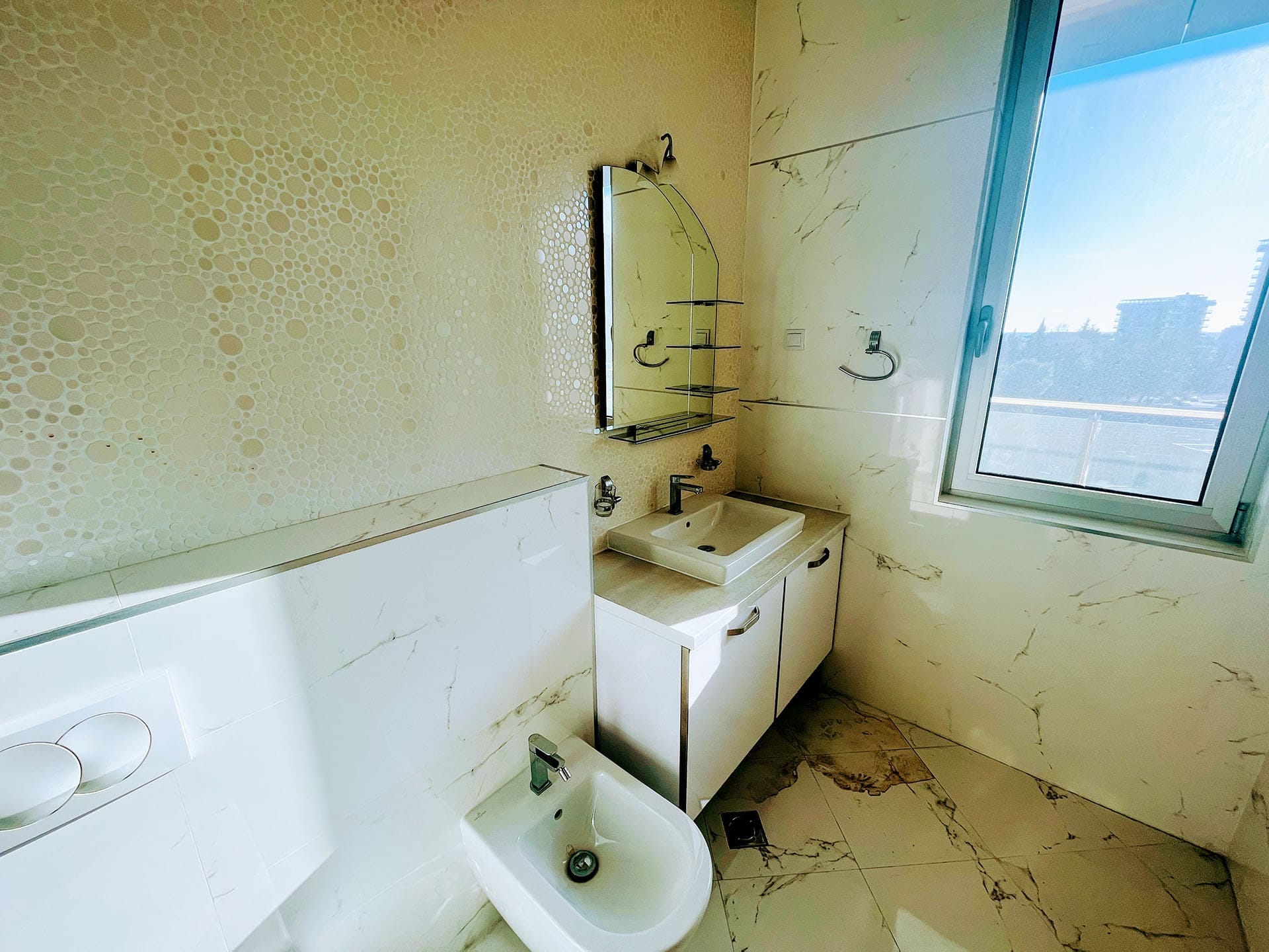 Budva, Karadağ’daki dairede bide ve pencereli modern banyo: mermer görünümlü fayans kaplama ve ayna.