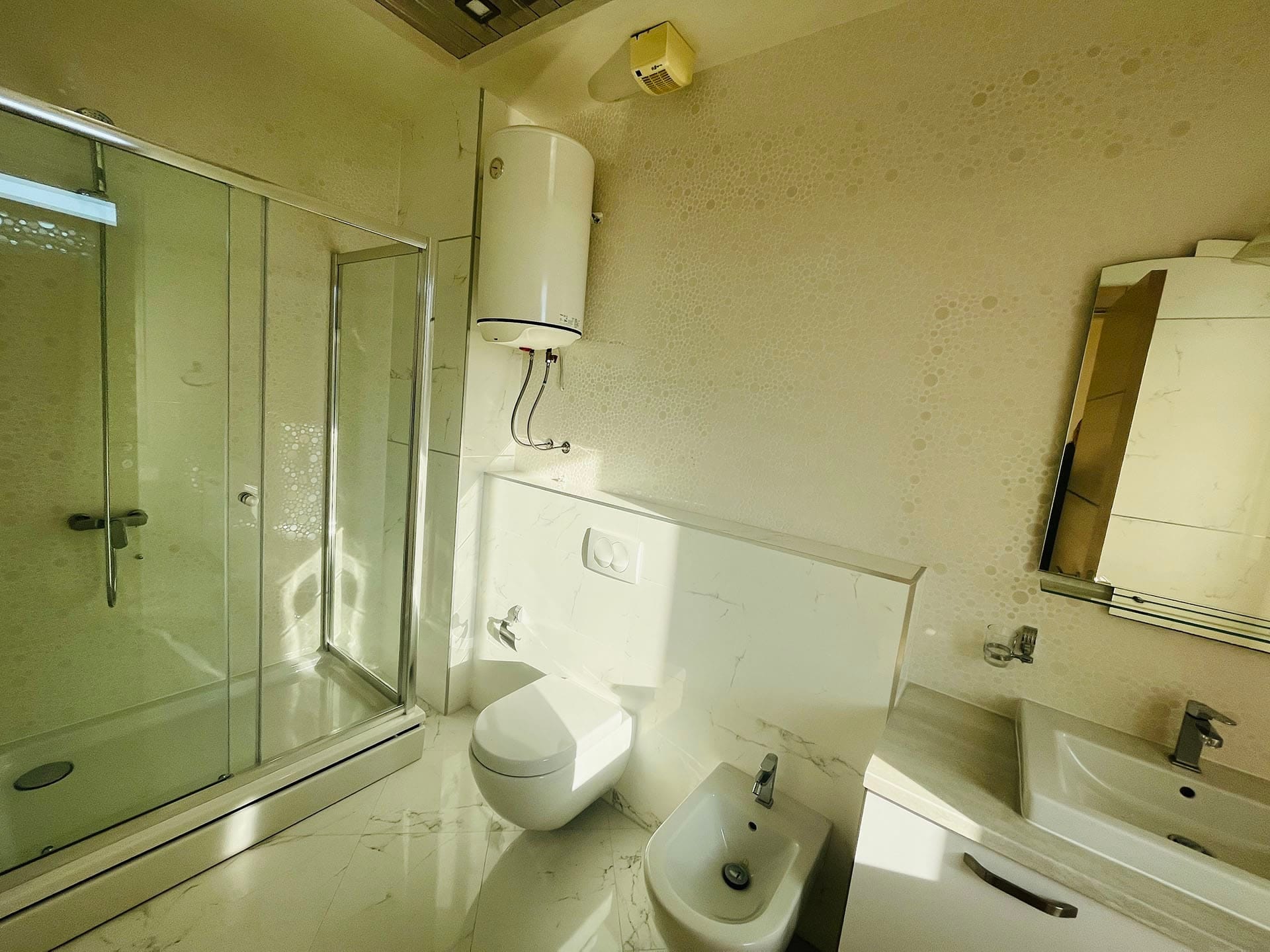Budva, Karadağ’daki dairede duş kabini ve bideli modern banyo: mermer görünümlü açık renkli kaplama.
