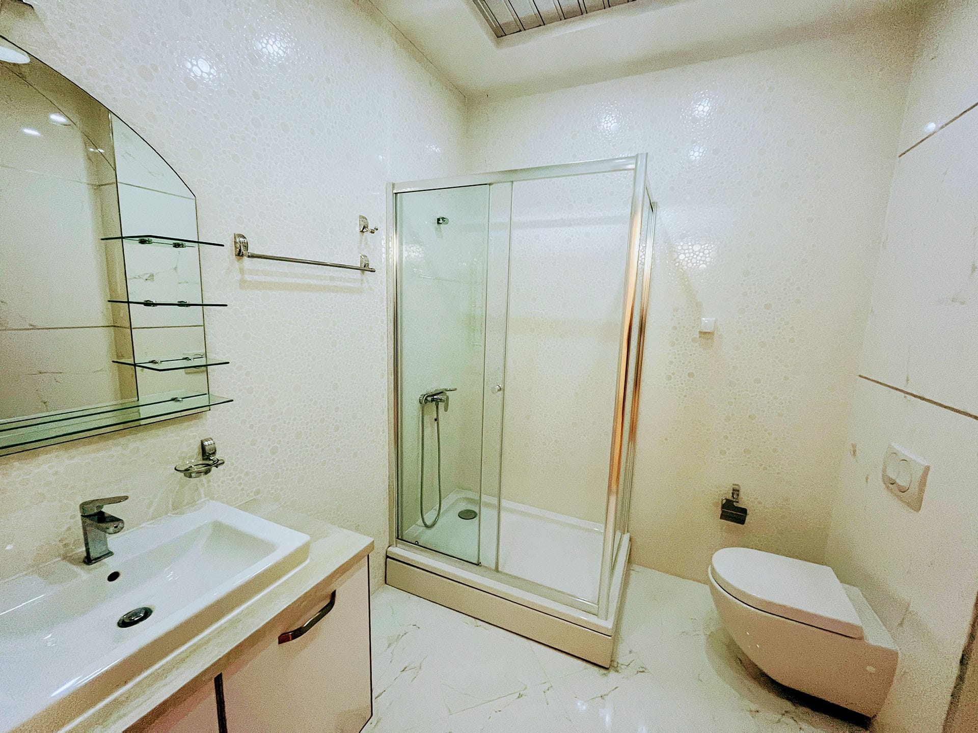 Karadağ, Budva’daki bir dairede modern banyo: duş kabini, asma klozet ve lavabolu dolap.