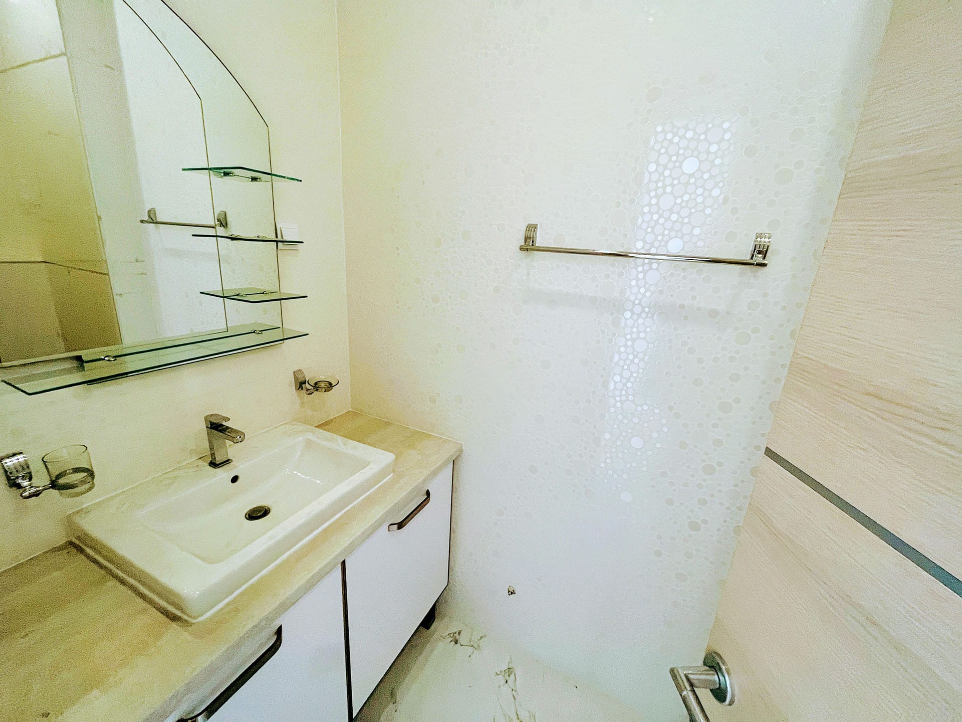 Budva, Karadağ’daki dairede aydınlık banyo: beyaz lavabolu dolap, ayna ve modern duvar kaplaması.