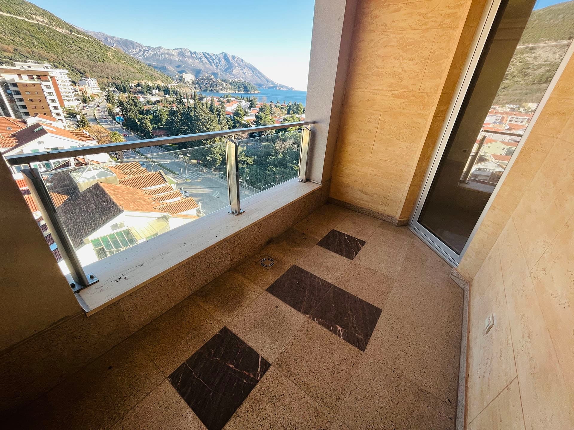 Budva, Karadağ’daki dairede balkon: deniz, dağlar ve şehrin panoramik manzarası, taş kaplama, cam korkuluk.