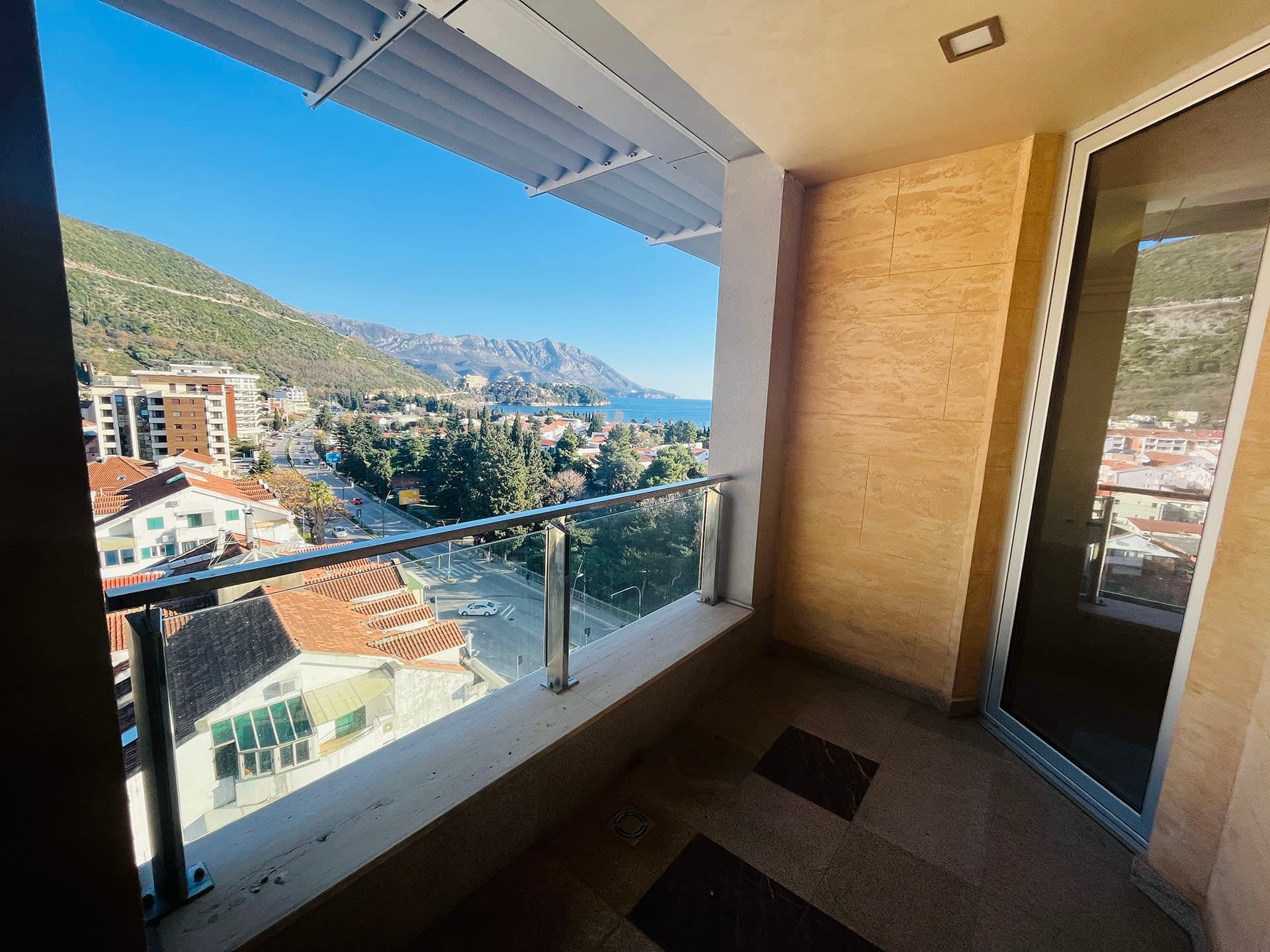 Budva, Karadağ’daki dairenin balkonu, deniz, dağlar ve şehre panoramik manzaralı, cam korkuluklu ve taş kaplamalı.