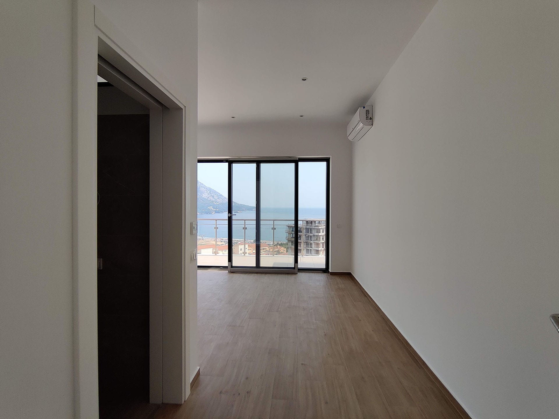 Svetao dnevni boravak u stanu u Bečićima, Crna Gora, sa panoramskim pogledom na more i planine kroz balkonska vrata.
