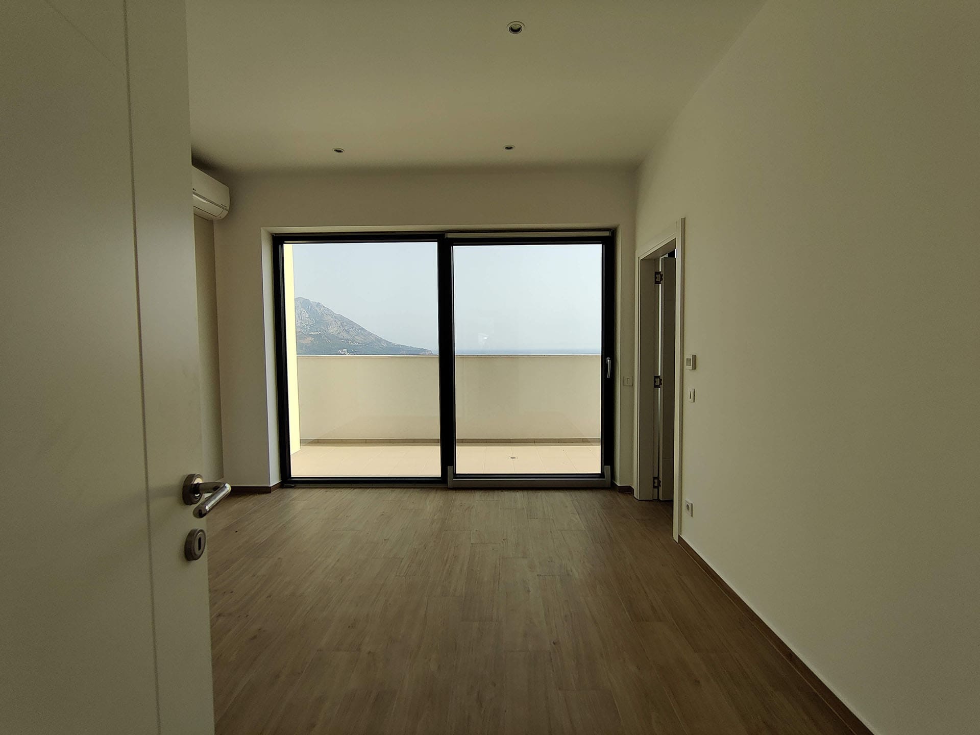 Svetao dnevni boravak u stanu u Bečićima, Crna Gora, sa panoramskim prozorom, izlazom na terasu i pogledom na more i planine.