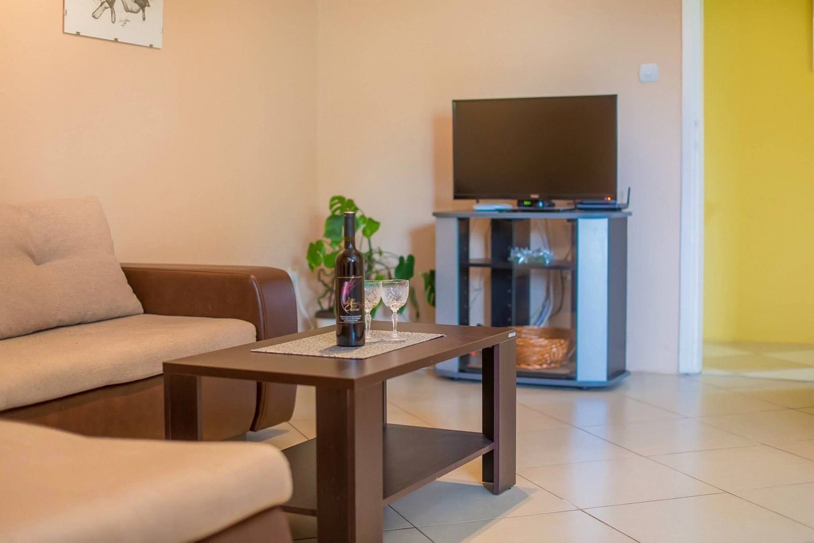 Cozy living room in an apartment in Dobrota, Montenegro: beige sofa, coffee table with wine, and a TV area with tile.