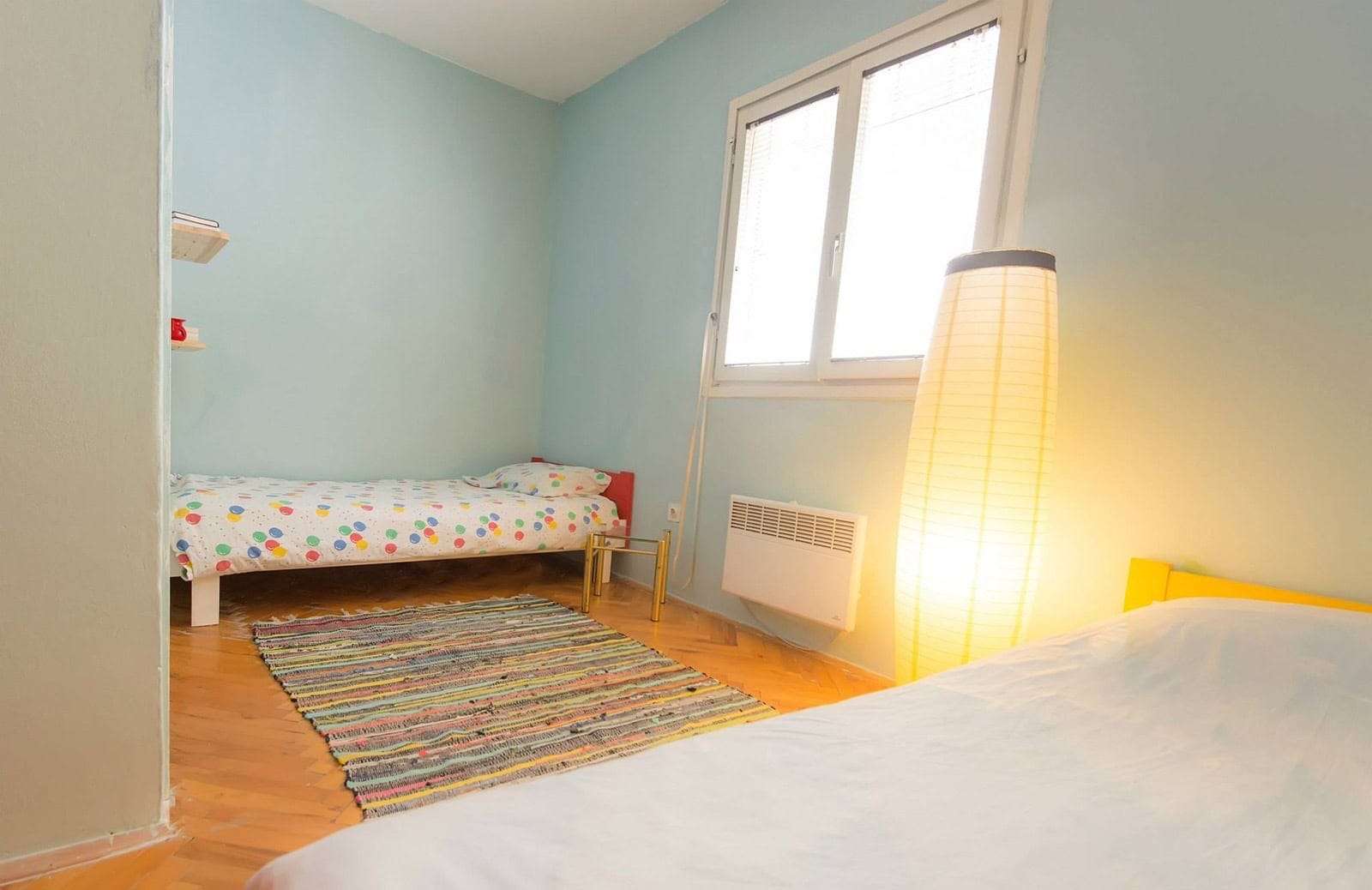 Bright bedroom with two beds, parquet flooring, and a floor lamp in an apartment for sale in Dobrota, Montenegro.