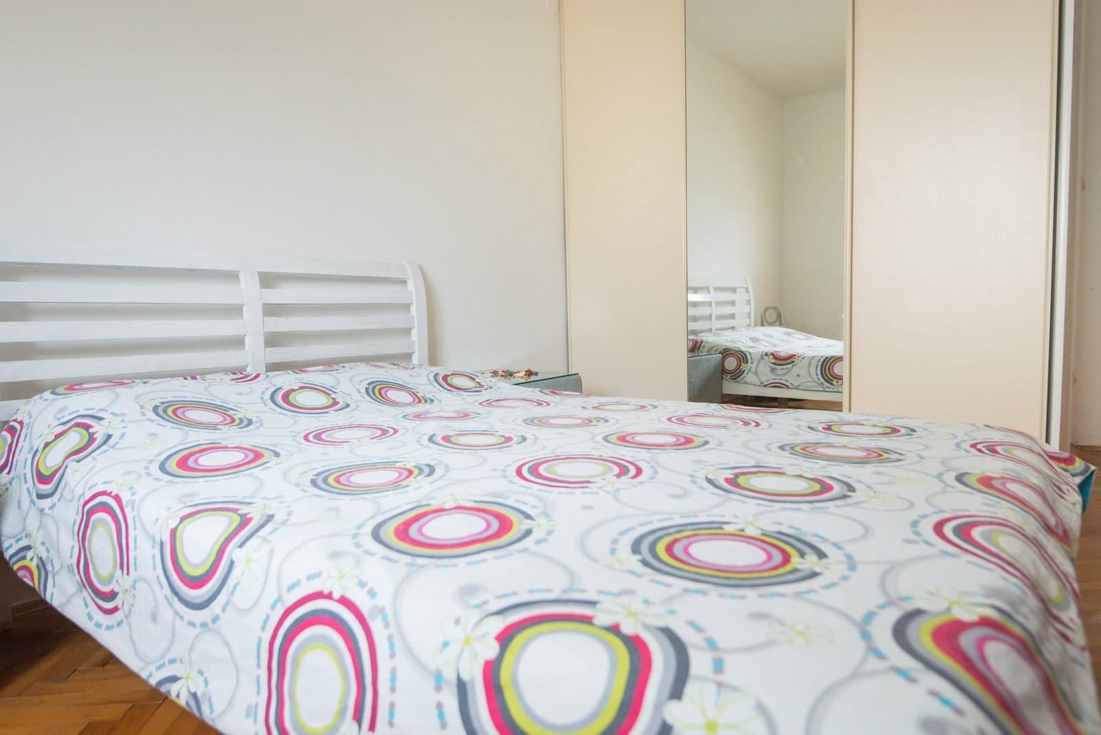 Bright bedroom with a white bed and mirrored sliding wardrobe in an apartment for sale, Dobrota, Montenegro.