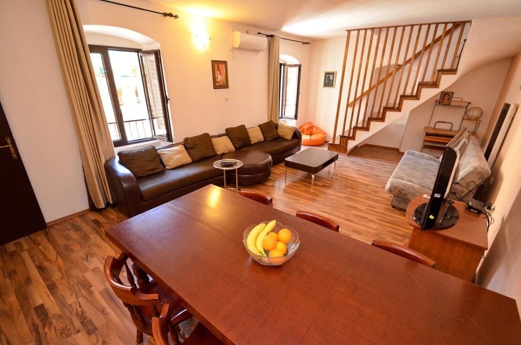 Living room with a wooden staircase and dining area in a house in Kotor, Montenegro: leather sofa and parquet floor.