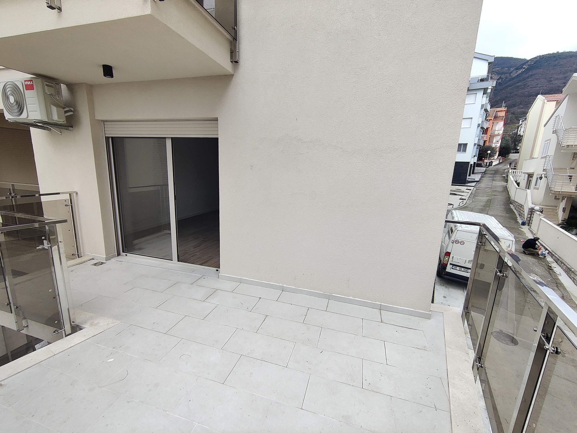 Prostran balkon sa panoramskim zastakljenjem u stanu, Bečići, Crna Gora: pogled na ulicu i planine, savremena završna obrada.