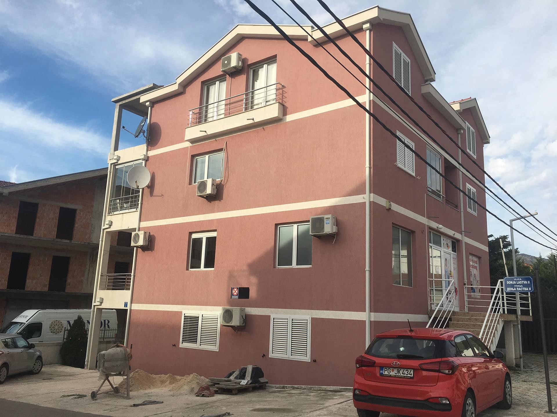 Trospratna stambena kuća roze boje u naselju Donja Lastva, Tivat, Crna Gora, sa parkingom i spoljnim klima uređajima.