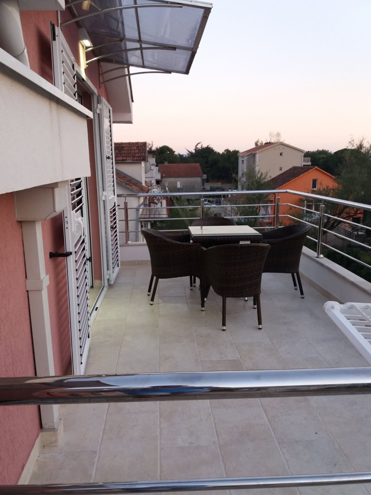 Prostran balkon sa pletenim nameštajem u stanu u Tivtu, Crna Gora, s pogledom na grad i krovove od crepa.