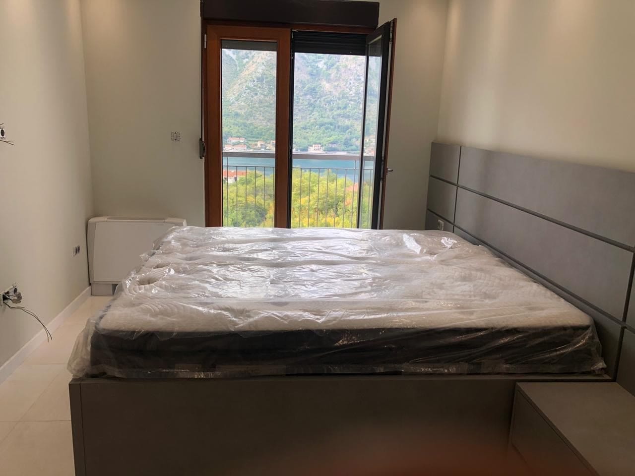 Spavaća soba u stanu u Dobroti, Crna Gora: bračni krevet, savremena završna obrada i pogled na more i planine iz prozora.