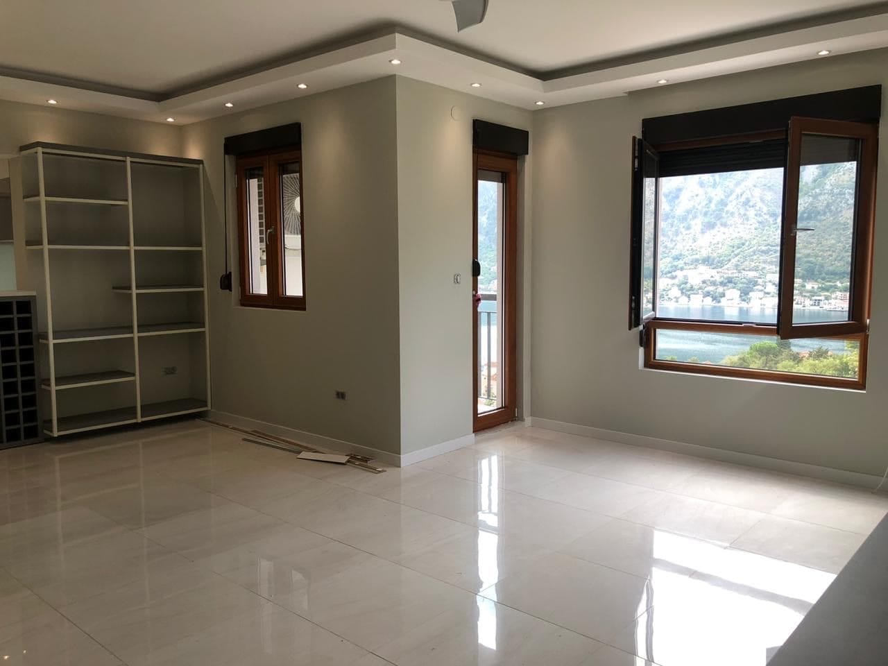 Svetla dnevna soba s panoramskim pogledom na Bokokotorski zaliv u stanu, Dobrota, Crna Gora: pločice, regal, izlaz na balkon