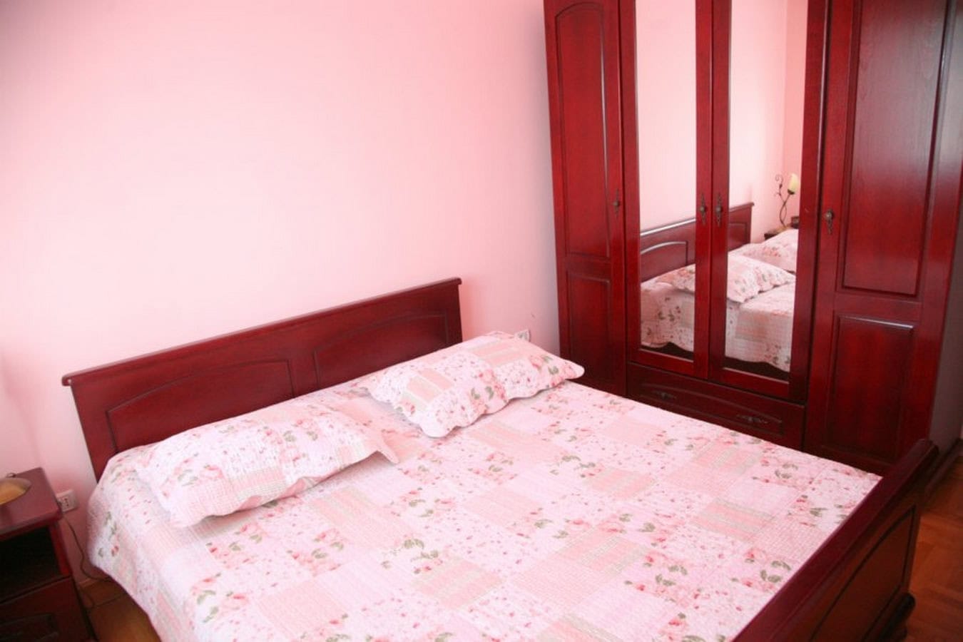 Schlafzimmer in einer Villa in Tivat, Montenegro: Doppelbett und Kleiderschrank aus dunklem Holz, rosa Wände, gemütliches Interieur.
