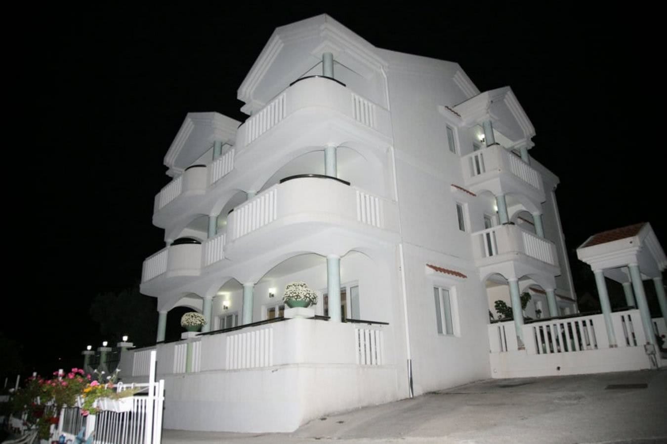 Dreistöckige weiße Villa in Tivat, Montenegro, mit offenen Balkonen und nächtlicher Fassadenbeleuchtung.