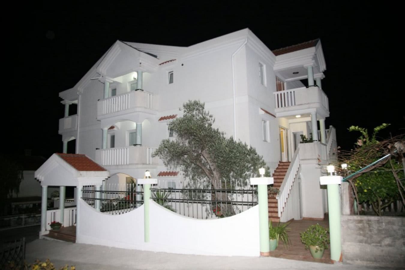 Dreistöckige weiße Villa in Tivat, Montenegro, mit Terrassen, Außentreppe und Zaun bei Nacht.