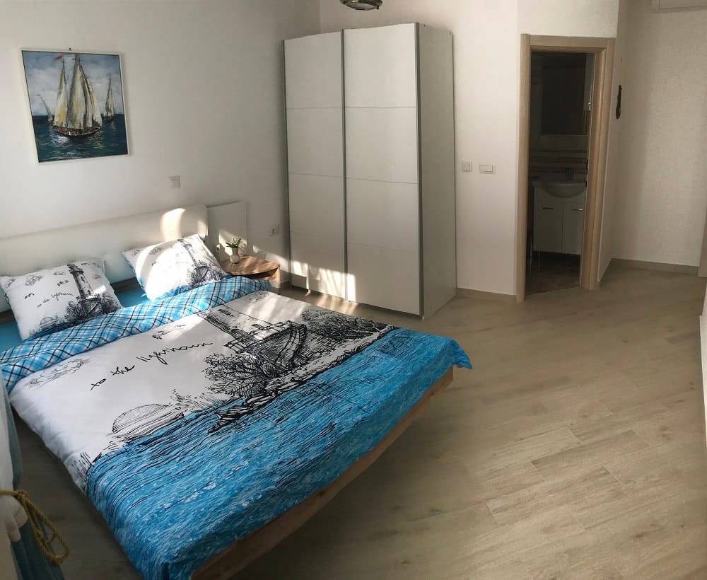 Helles Schlafzimmer in einer Wohnung, Dobri Vody, Montenegro: Doppelbett, weißer Kleiderschrank und separates Badezimmer.
