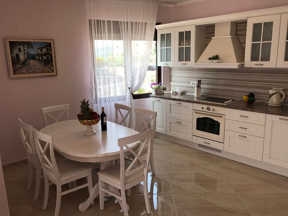 Helle Wohnküche mit weißen Möbeln in einer Wohnung in Dobri Vody, Montenegro: Esstisch und moderne Geräte.